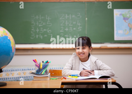 Smiling schoolgirl s'appuyant sur un livre de coloriage Banque D'Images