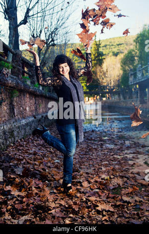 Belle jeune fille se jette dans l'air un tas de feuilles en automne. Banque D'Images