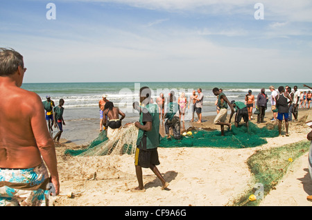 Les vacanciers se mêler aux pêcheurs locaux comme il se hisse dans leurs filets sur la plage de Kololi Gambie Afrique de l'ouest Banque D'Images