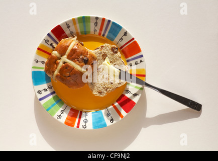 Beurrer un hot cross bun sur plaque colorée prête pour Pâques isolé sur fond blanc Banque D'Images