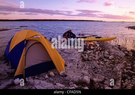 Les campeurs profitez d'un feu de camp à côté de leur kayak, au coucher du soleil, sur la rive du lac Huron, en Ontario, Canada. Banque D'Images