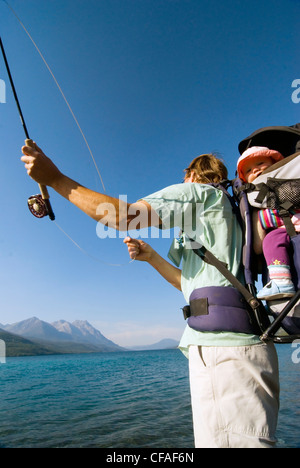 Père pêcheur avec fille en porte-sac à dos pour enfants, pêche à la mouche pour la truite, Tatlayoko Lake, British Columbia, Canada. Banque D'Images