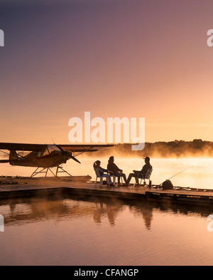 Silhouette of family sitting on dock hydravion le matin, la rivière Rouge, Manitoba, Canada Banque D'Images