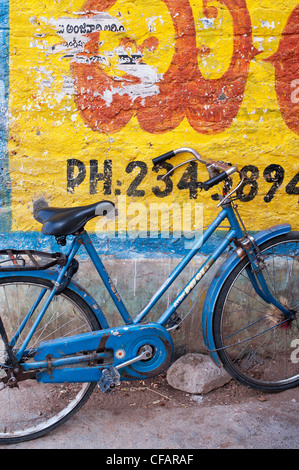 Womans indien traditionnel vélo contre un mur peint en jaune. L'Andhra Pradesh, Inde Banque D'Images