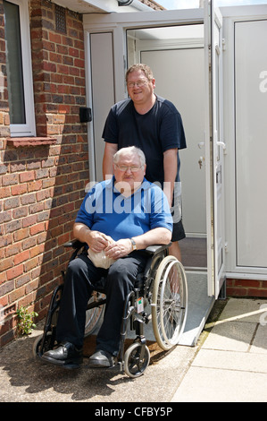 Mobilité un homme âgé en fauteuil roulant avec son fils soignant devant leur porte d'entrée Banque D'Images