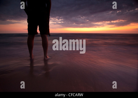 L'homme regarde le soleil se coucher sur le lac Huron en étant debout dans l'eau sur la plage de Grand Bend, Ontario Banque D'Images