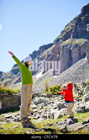 Les vagues d'une mère ses mains en l'air tandis qu'elle marche avec son fils de 2 ans par le biais d'un pré alpin avec wildflower. Ils ar Banque D'Images