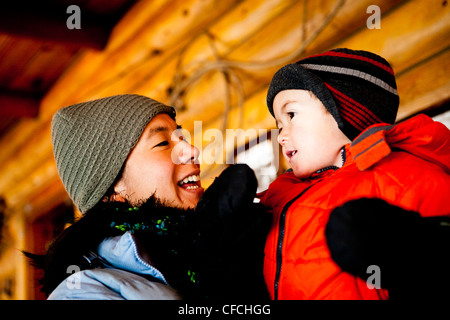Une femme est emmitouflé dans des vêtements chauds et stock cap / hat dans un tout en maintenant son fils dans une cabane. Banque D'Images