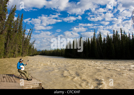Kayakiste féminine prend une pause de barbotage pour jouer son banjo le long de la rivière Athabasca, Jasper National Park, Alberta, Canada Banque D'Images