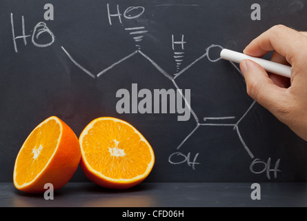 Dessin à la main la formule chimique de la vitamine C sur tableau noir avec des oranges à l'avant Banque D'Images