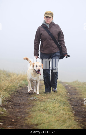 Femme promener son chien Labrador Retriever jaune sur un jour brumeux, pluvieux. Nose Hill Park, Calgary, Alberta, Canada. Banque D'Images