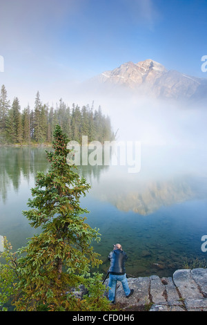 Photographe sur les rives du lac Pyramid Pyramid Mountain avec partiellement obscurci par la brume, Jasper National Park, Alberta, Canada Banque D'Images