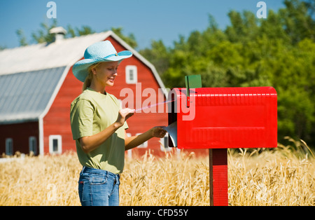 Une fille vérifie une boîte aux lettres rurale en face d'un champ de blé de printemps et de basse-cour, Grande Pointe, au Manitoba, Canada Banque D'Images