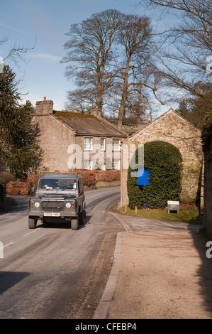 Vue avant du Land Rover Defender en voyage ou en roulant sur route de campagne passé quaint cottage - Saint-cergue village, North Yorkshire, Angleterre, Royaume-Uni. Banque D'Images