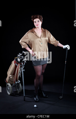 La femme pose élégamment vêtu avec des clubs de golf en face de toile noire Banque D'Images