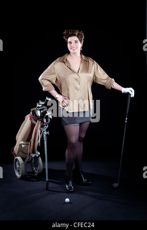 La femme pose élégamment vêtu avec des clubs de golf en face de toile noire Banque D'Images