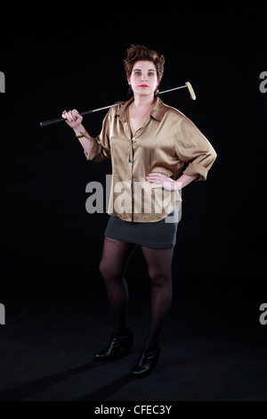 La femme pose élégamment vêtu avec des clubs de golf en face de toile noire Banque D'Images