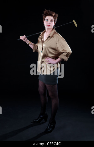 Élégamment vêtue femme pose avec un club de golf en face de toile noire. Banque D'Images