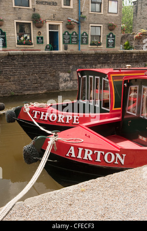 Face à 2 bateaux de canal rouge vif (noms sur l'arc) amarré côte à côte par le chemin de remorquage et le pub canalside - Canal Leeds-Liverpool, Skipton, Yorkshire, Angleterre. Banque D'Images