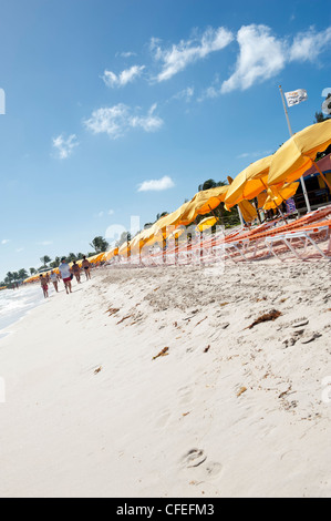 Les gens qui marchent le long de la côte d'Orient Bay Saint Martin, avec parasols jaunes Banque D'Images