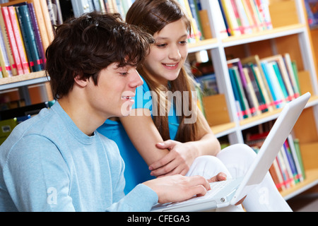 Guy at bibliothèque tandis que sa petite amie à la recherche à l'écran avec un sourire Banque D'Images