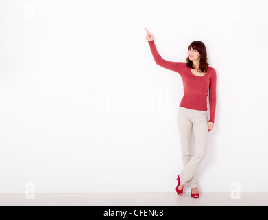 Belle jeune femme en pointant sur le côté droit avec copyspace, contre un mur blanc Banque D'Images