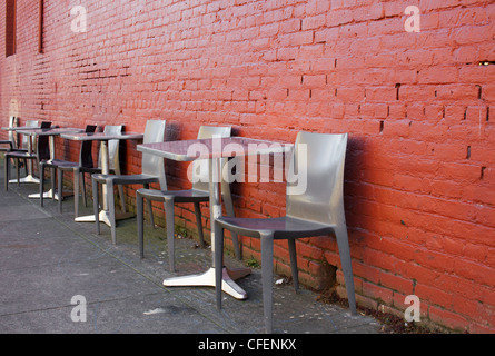 Tables et chaises en aluminium brossé sur un sidwalk contre un mur de brique rouge Banque D'Images