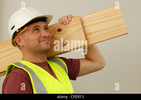 Un ouvrier pose modèle wearing hard-hat, hi-vis jacket et crayon derrière l'oreille Banque D'Images