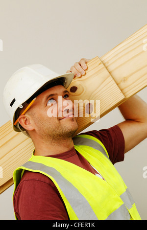 Un ouvrier pose modèle wearing hard-hat, hi-vis jacket et crayon derrière l'oreille Banque D'Images