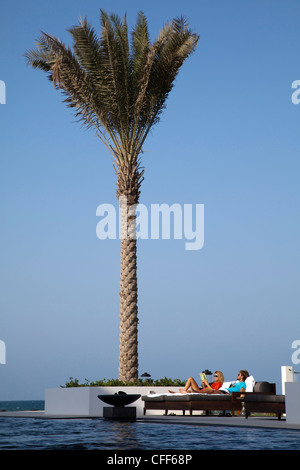 Couple détend près de palm tree, la piscine, l'hôtel The Chedi Muscat, Muscat, Mascate, Oman, Péninsule Arabique Banque D'Images