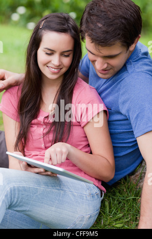 Jeune beau couple assis dans un parc tout en regardant un tablet pc Banque D'Images