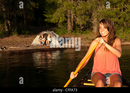 Une jeune femme sourit tout en canoë sur un voyage de camping au bord d'un lac dans l'Idaho. Banque D'Images