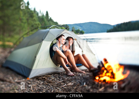 Un jeune couple rire et sourire assis dans leur tente à côté d'un feu de camp dans l'Idaho. Banque D'Images