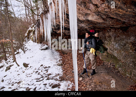 Un jeune homme se repose de la randonnée dans la neige et de la glace sous le couvert d'une saillie rocheuse. Banque D'Images