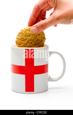 Main caucasienne dounant un biscuit dans une tasse blanche avec croix rouge St Georges sur le côté. Banque D'Images