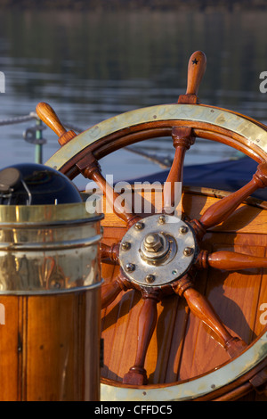 Une lueur chaude met en lumière le gouvernail et la boussole à bord d'un yacht à voile classique au coucher du soleil. Banque D'Images