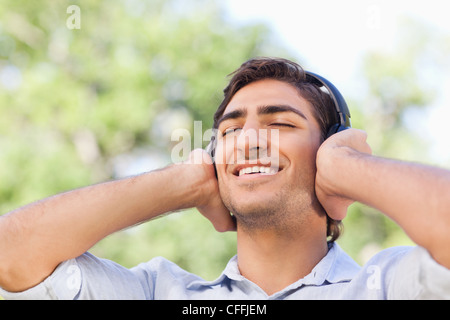 Smiling man enjoying music dans le parc Banque D'Images