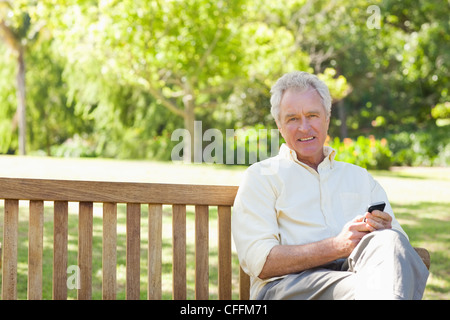 L'homme cherche dans la distance tout en tenant un téléphone comme il est assis sur un banc Banque D'Images