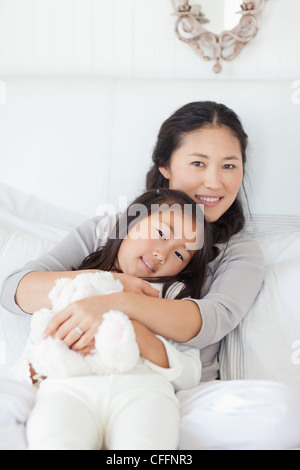 Une mère tient son enfant dans ses bras qu'elle détient sur un ours, assis sur le lit Banque D'Images