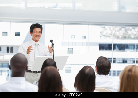 Businessman smiling comme il les gestes pour un public qui sont le regarder Banque D'Images