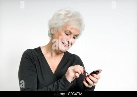 Attractive senior dame souriant à l'aide de téléphone mobile prises sur un fond blanc. Banque D'Images