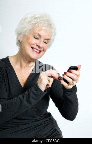 Attractive senior dame souriant à l'aide de téléphone mobile prises sur un fond blanc. Banque D'Images