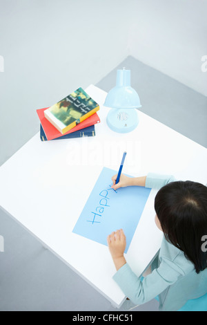 Une fille écrit 'Happy' sur le papier bleu avec un crayon de couleur bleu Banque D'Images