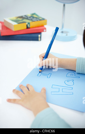 Une fille écrit 'Je suis heureux' sur le papier bleu avec un crayon de couleur bleu Banque D'Images