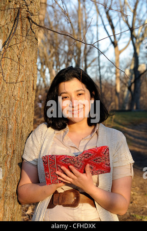 Hispanic woman in park au cours des derniers jours de l'hiver, la lecture d'un livre. Banque D'Images
