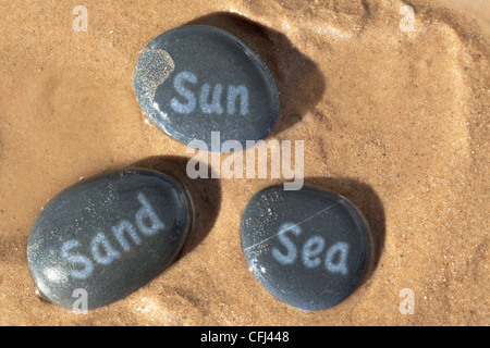 Concept photo de Sun Sand et écrit sur la mer de cailloux humides sur la plage avec le soleil d'ombres profondes. Banque D'Images