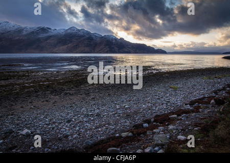 Plage de galets sur les rives du Loch Hourn en fin d'après-midi avec des montagnes enneigées de l'île de Skye, dans l'arrière-plan Banque D'Images