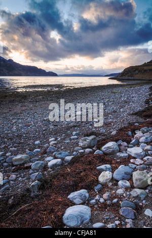 Plage de galets sur les rives du Loch Hourn en fin d'après-midi avec des montagnes enneigées de l'île de Skye, dans l'arrière-plan Banque D'Images