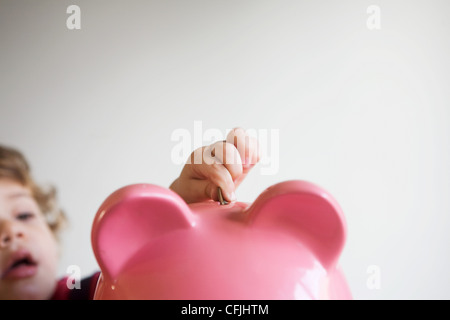 Little Boy putting money in piggy bank Banque D'Images