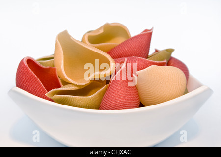 De grandes coquilles de pâtes colorées séchées dans un bol blanc sur un fond blanc. Banque D'Images